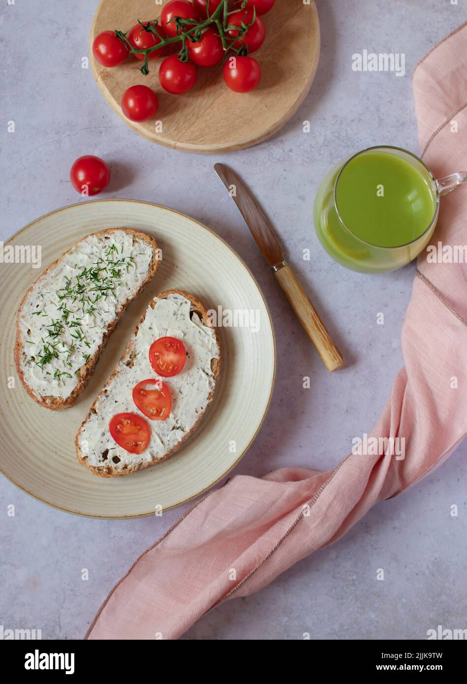 Ein Teller mit einem gesunden skandinavischen „Mororgas“ oder „Morrebrod“-Frühstück mit offenem Sandwich. Mit Frischkäse, Smoothie, frischen Campari-Tomaten und Dill. Stockfoto