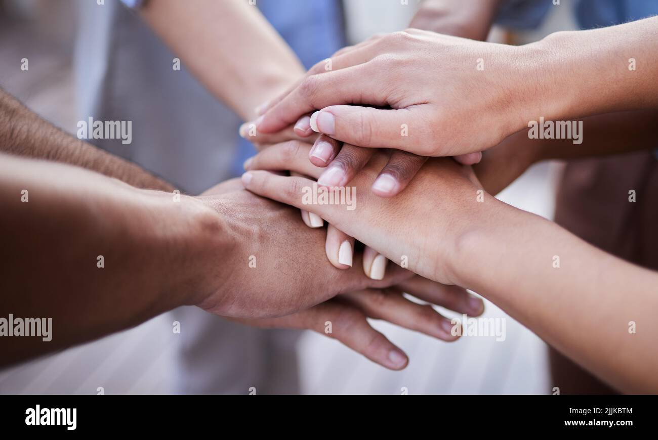 Dies ist eine Teamarbeit. Eine nicht erkennbare Gruppe von Geschäftsleuten, die zusammen mit ihren Händen in der Mitte gestapelt stehen. Stockfoto