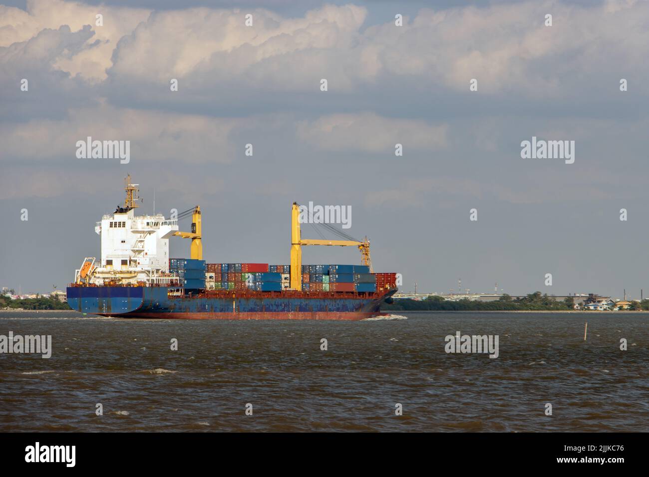 Das Containerschiff, das mit Containern beladen ist, fährt an einer Küste entlang Stockfoto