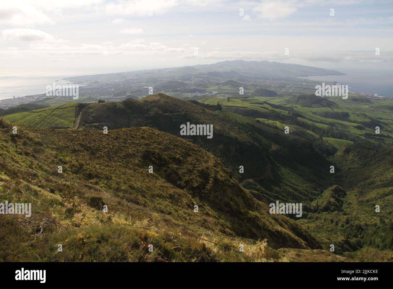 Eine Luftaufnahme von Hügeln, die an einem bewölkten Tag mit viel Grün bedeckt sind, gegen die Meereslandschaft Stockfoto