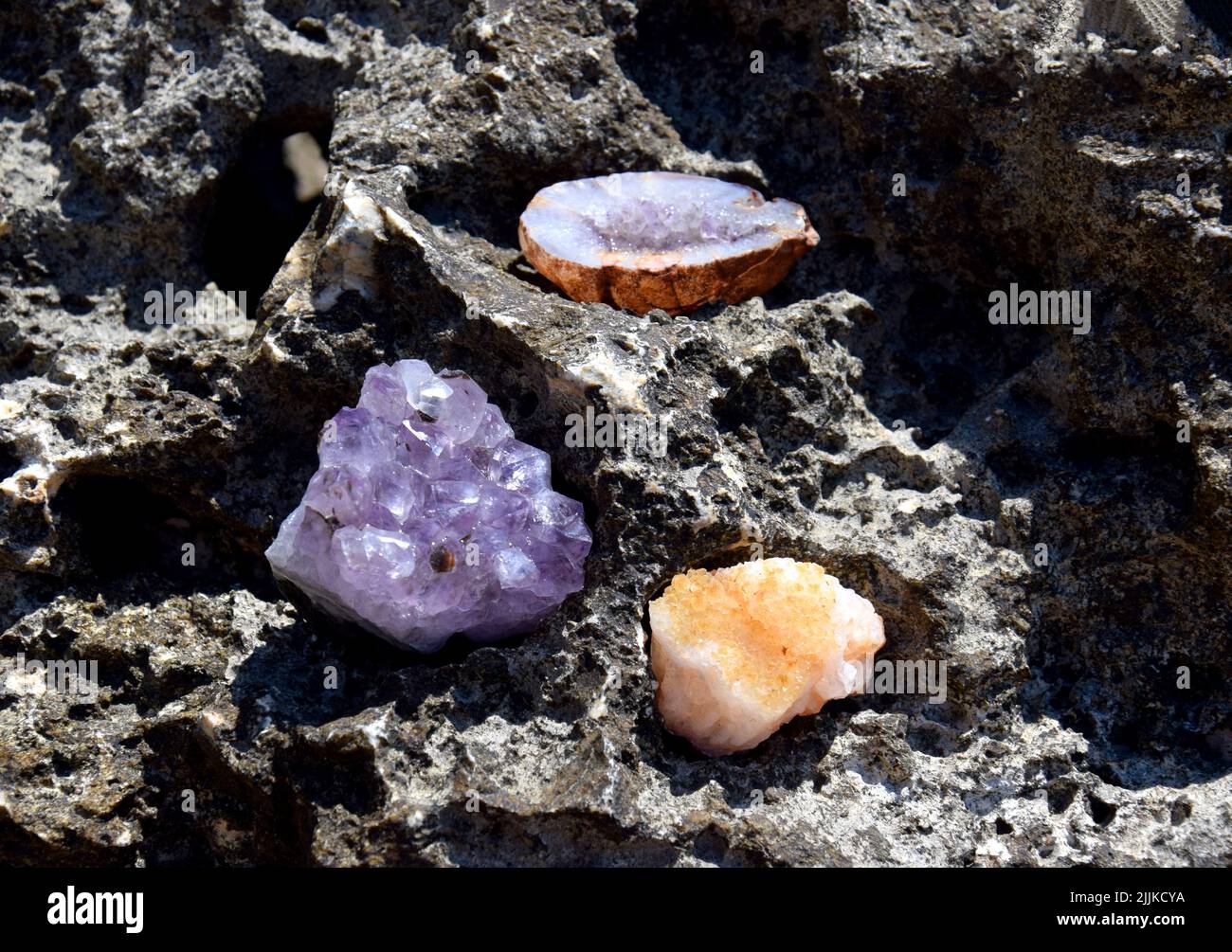 Eine schöne Druse und Geode aus Amethyst und Druse aus Citrin liegen auf einem Stein. Kristalle von Halbedelsteinen in der Sonne. Stockfoto