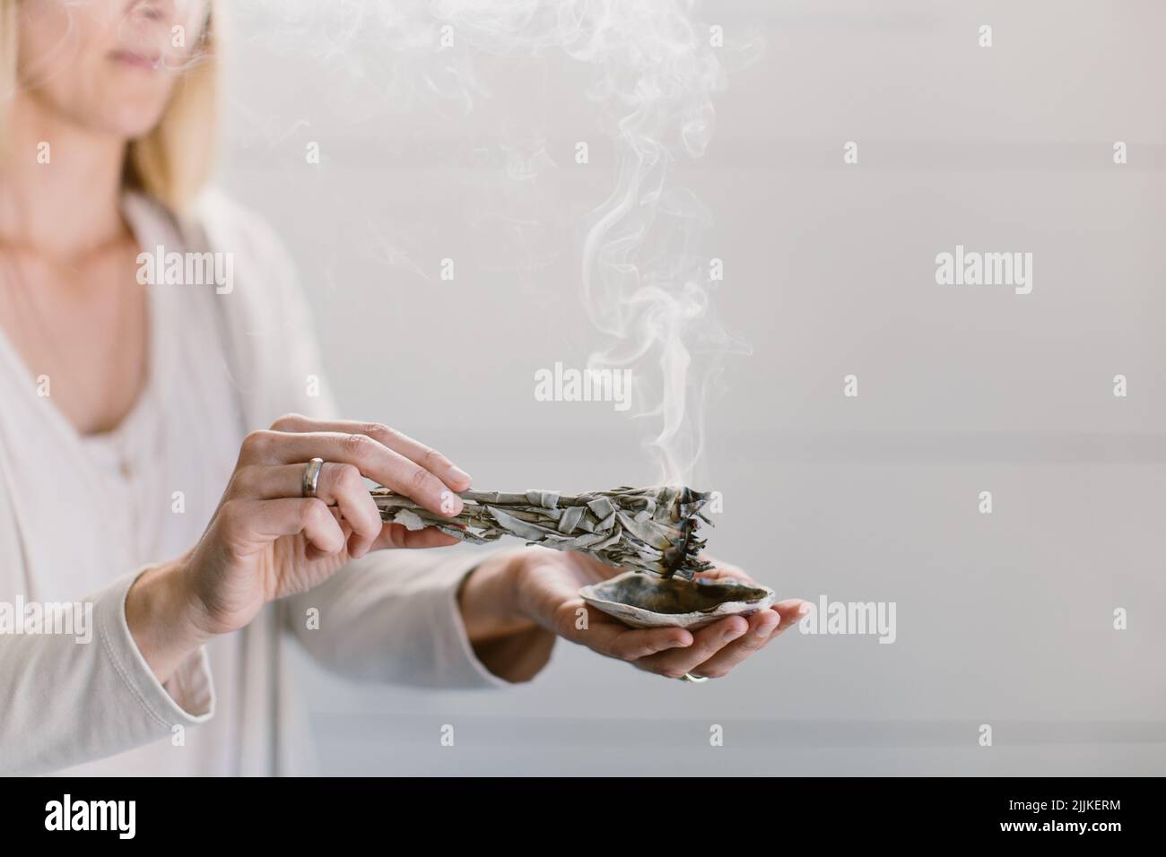 Eine Frau, die Salbei verbrennt und ihn über eine Muschel hält. Stockfoto