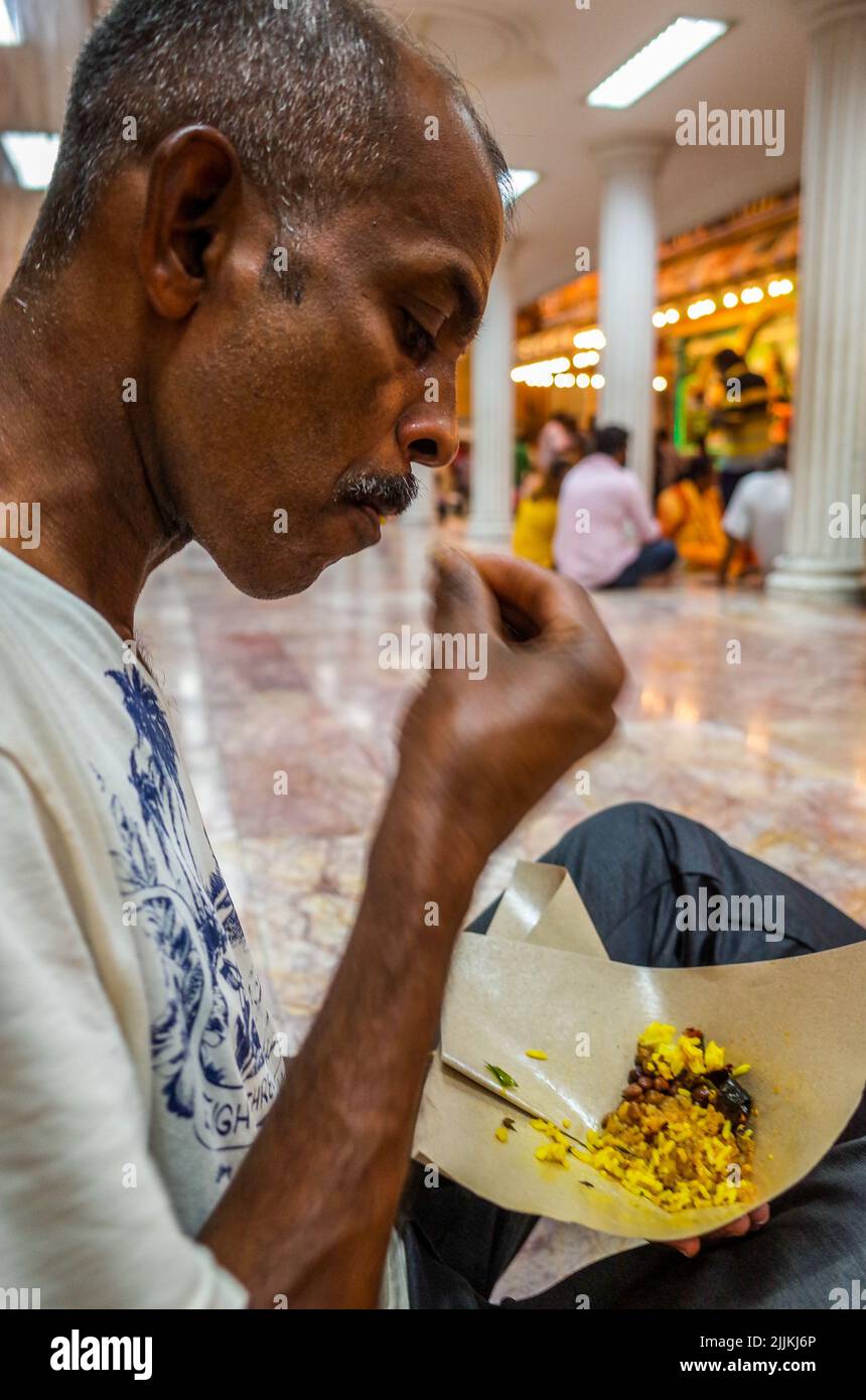 Nahaufnahme eines Mannes mittleren Alters mit einem Schnurrbart, der auf dem Boden sitzt und Essen isst Stockfoto