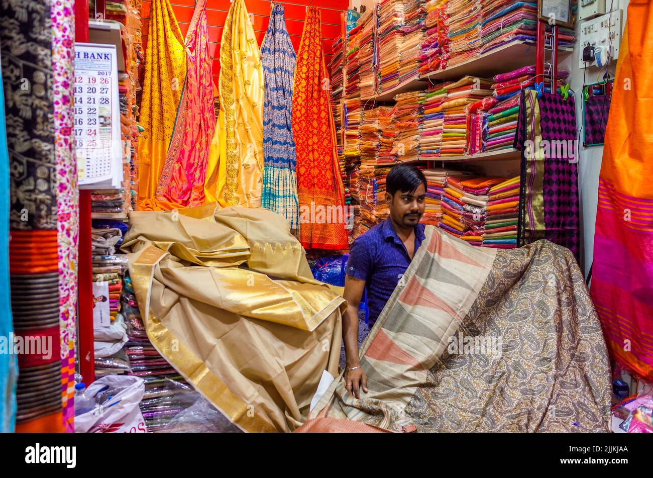 Eine Aufnahme eines indischen Mannes, der in einem Laden voller lebhafter Kleidung steht Stockfoto