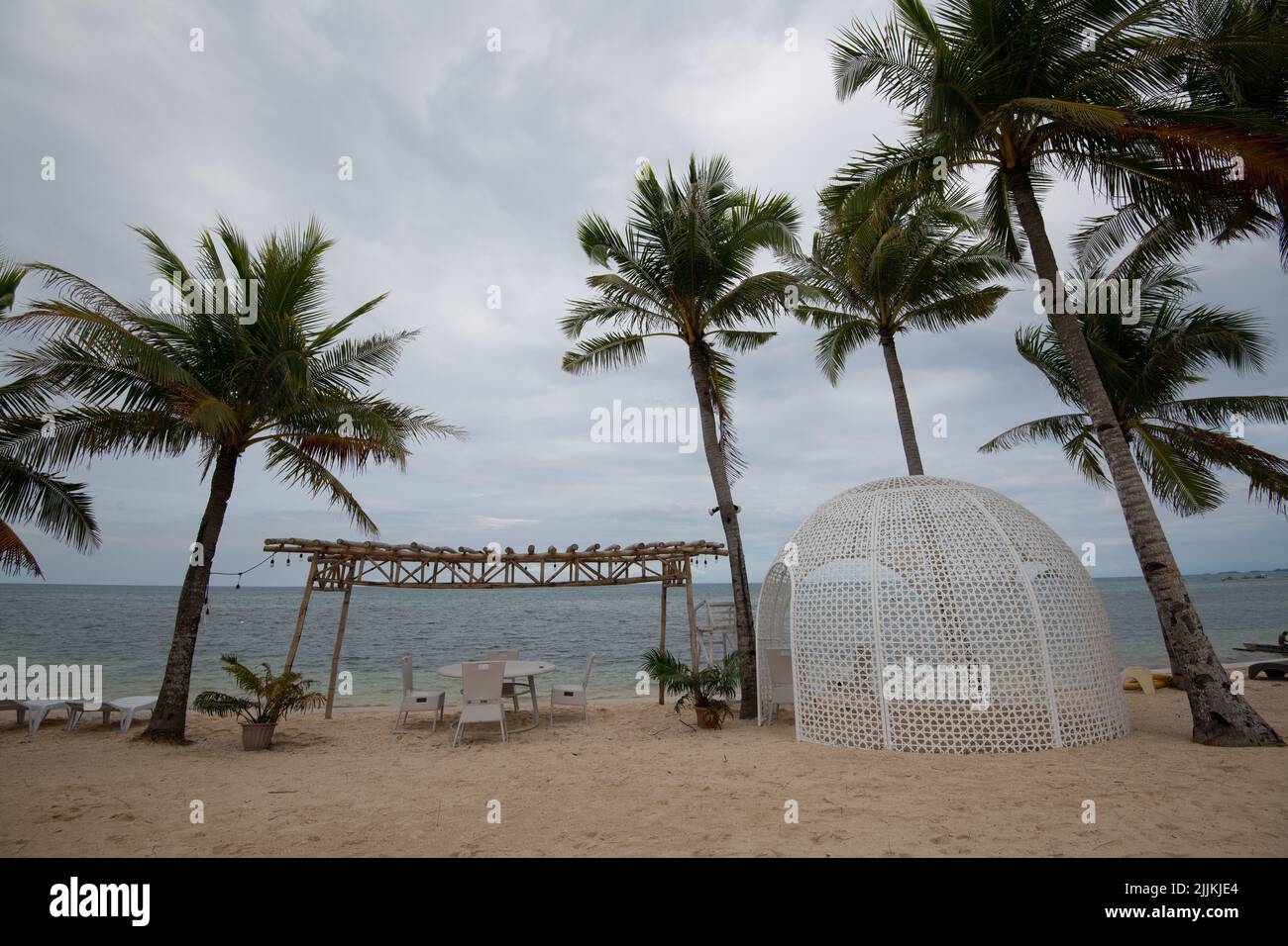 Ein Sandstrand mit Palmen und ein Café im Freien an einem bewölkten Tag Stockfoto