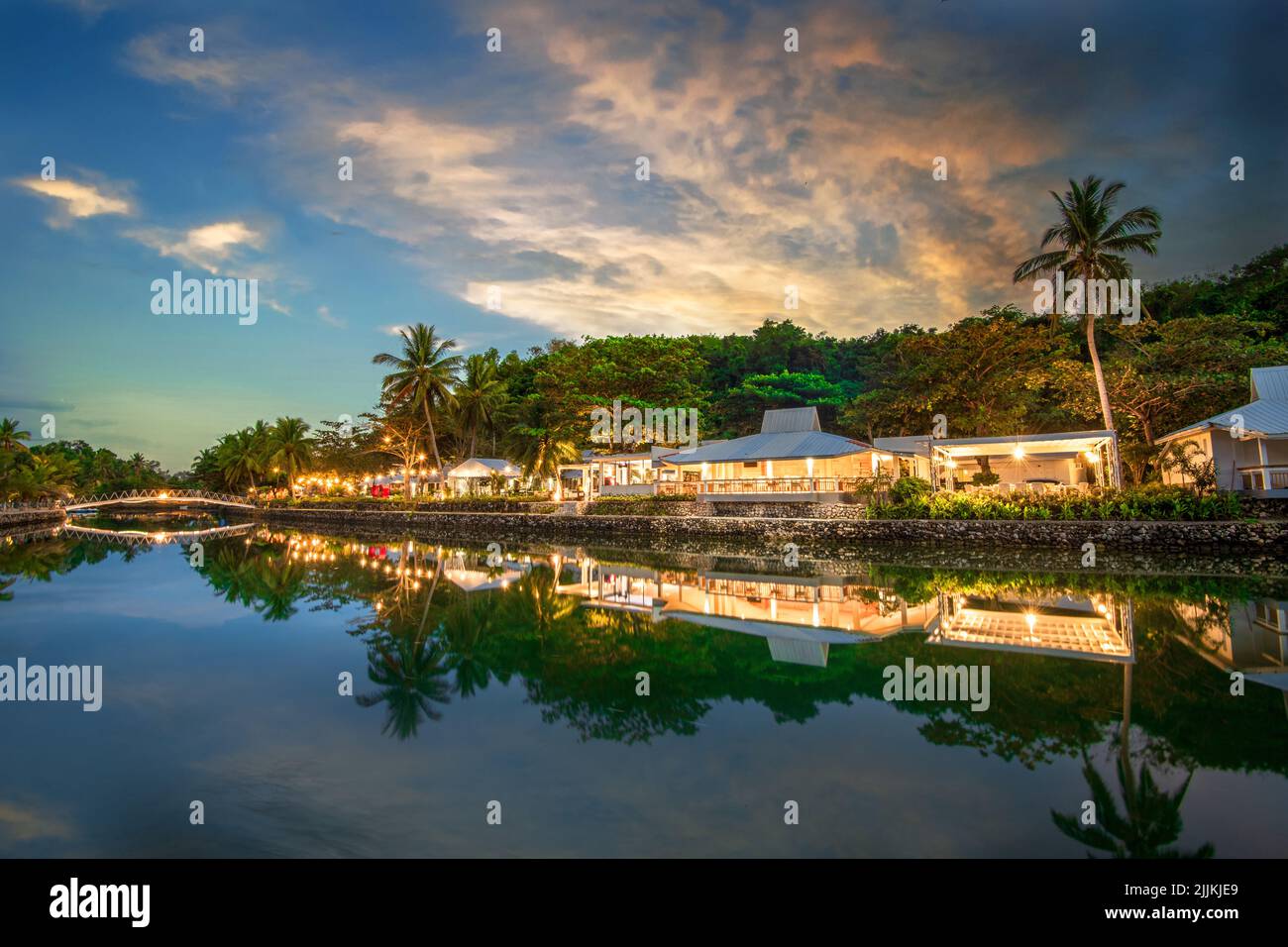 Ein Fernblick auf das wunderschöne Resort mit Gebäuden und Bäumen, die sich während des Sonnenuntergangs im Wasser spiegeln Stockfoto