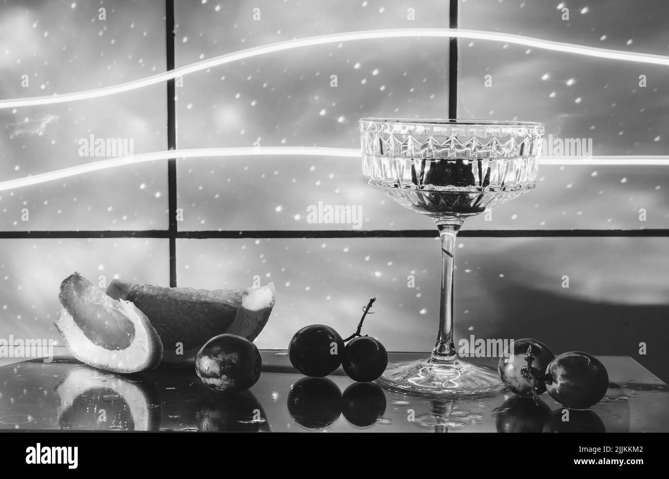 Kristallglas für Cocktails auf einer Glasoberfläche. Früchte - Trauben, Grapefruit neben dem Glas. Abstrakter Hintergrund. Stockfoto