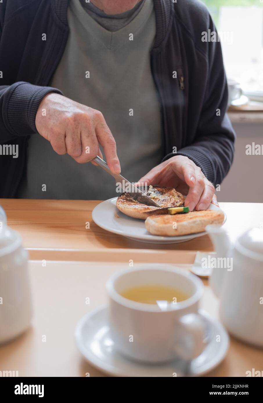 Reifer Mann, der einen gerösteten Teetake schlachtet und in der Mittagspause Tee mit Freunden in einem Café genießt. Eine Teekannen und eine Tasse grüner Tee im Vordergrund. Stockfoto