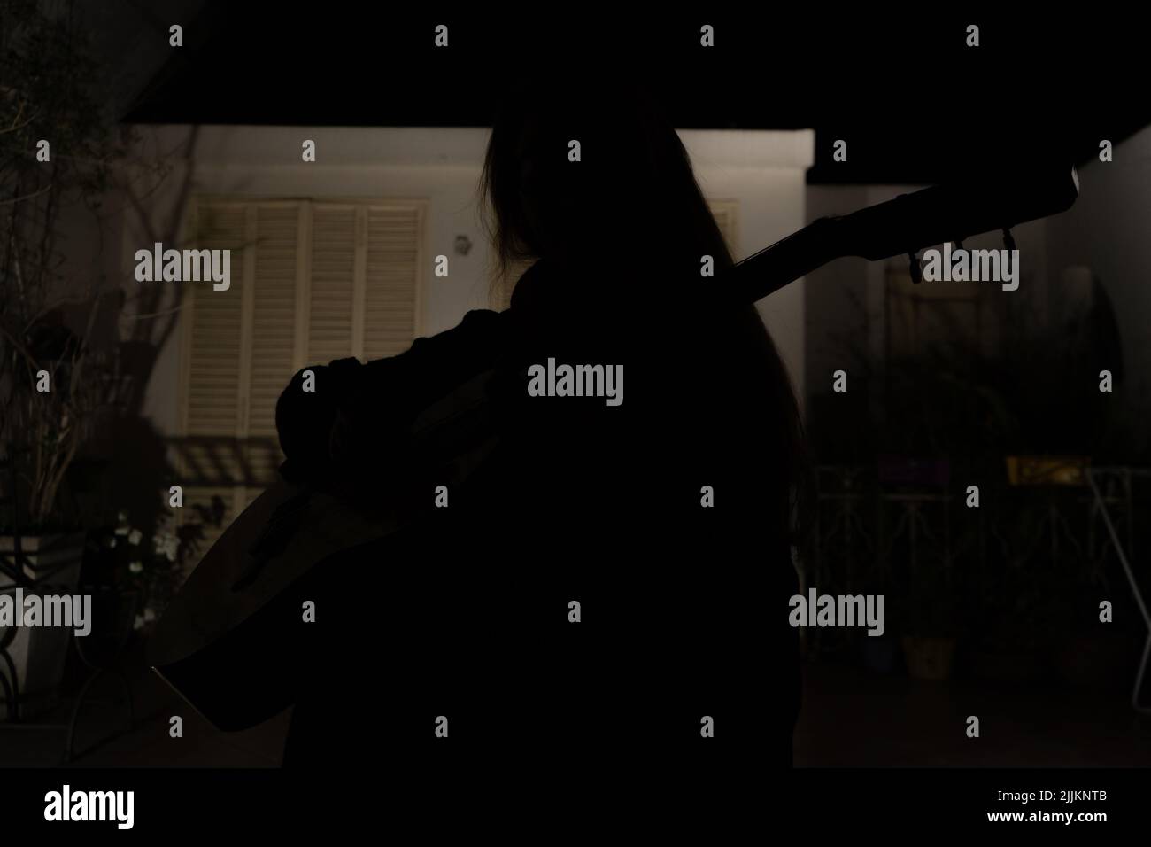 Frontansicht der Silhouette einer Person im Dunkeln, die mit einer Hintergrundbeleuchtung die Gitarre spielt Stockfoto