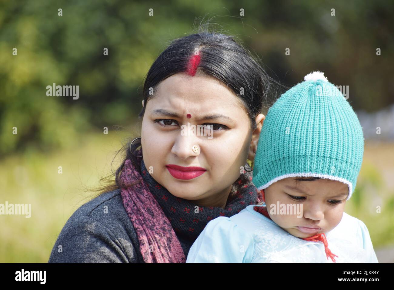 Eine seichte Fokusaufnahme einer südostasiatischen Frau mit einem Bindi und Nasenpiercing, das ein Baby in einem Gr hält Stockfoto