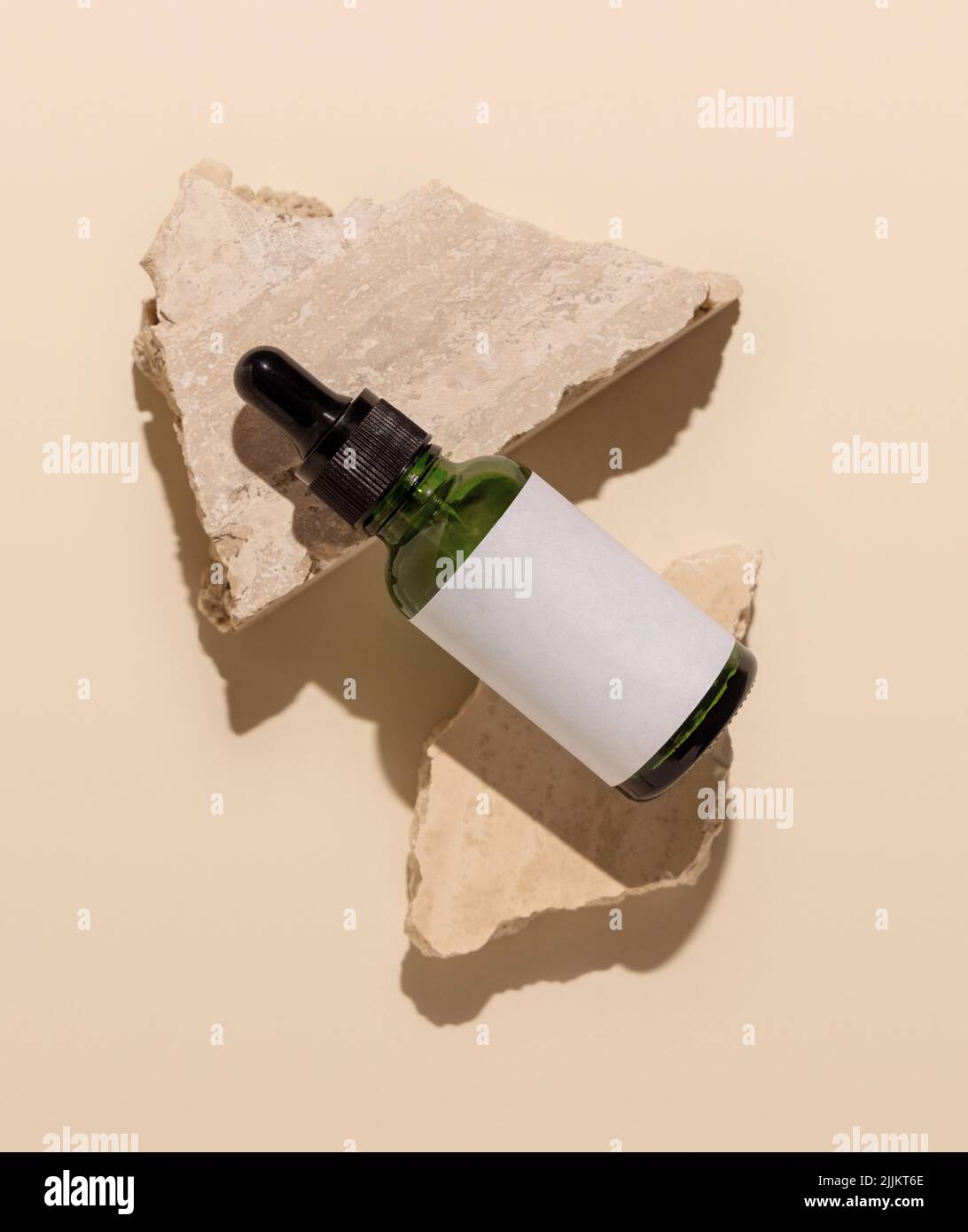 Grüne Glasflasche liegt auf beigefarbenen Travertin-Steinen auf hellgelber Draufsicht, Mockup. Hautpflege Beauty-Produkt-Paket. Naturkosmetik, Minim Stockfoto