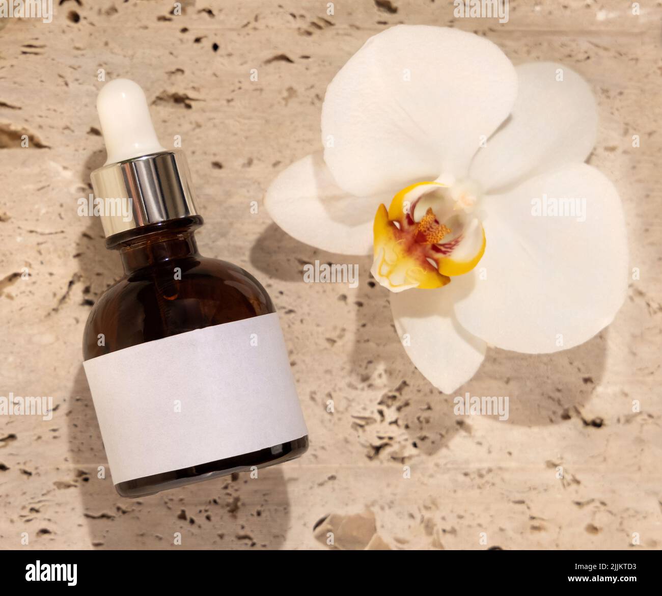 Braune Glasflasche auf Stein in der Nähe der weißen Orchideenblume Draufsicht, Etikett Mockup. Hautpflege handgemachtes Beauty-Produkt, Serum oder Lotion. Exotisch natürlich Stockfoto