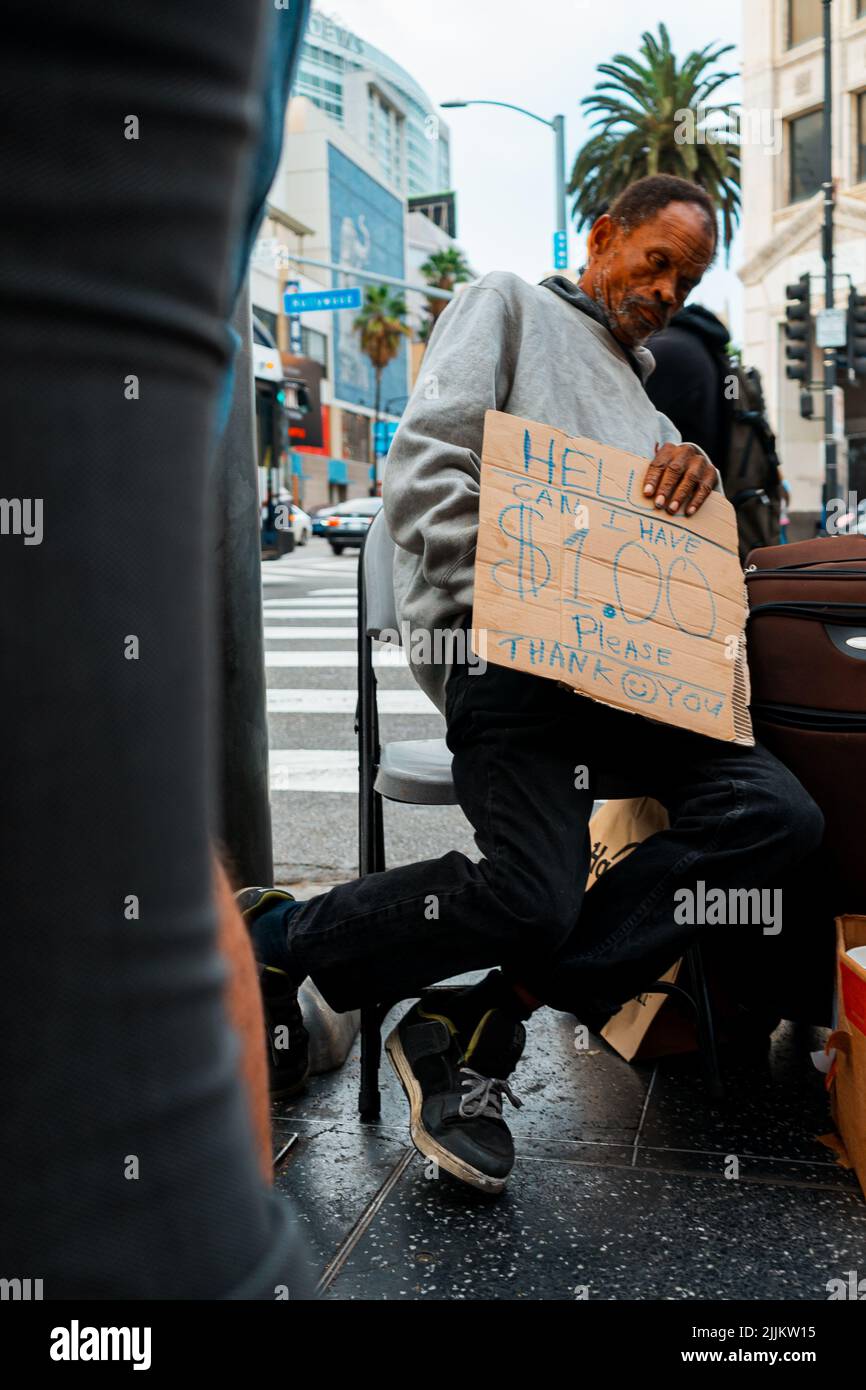 Die vertikale Aufnahme eines obdachlosen schwarzen älteren Mannes, einer Obdachlosen, die ein Schild mit der Bitte um Geld in der Hand hält Stockfoto