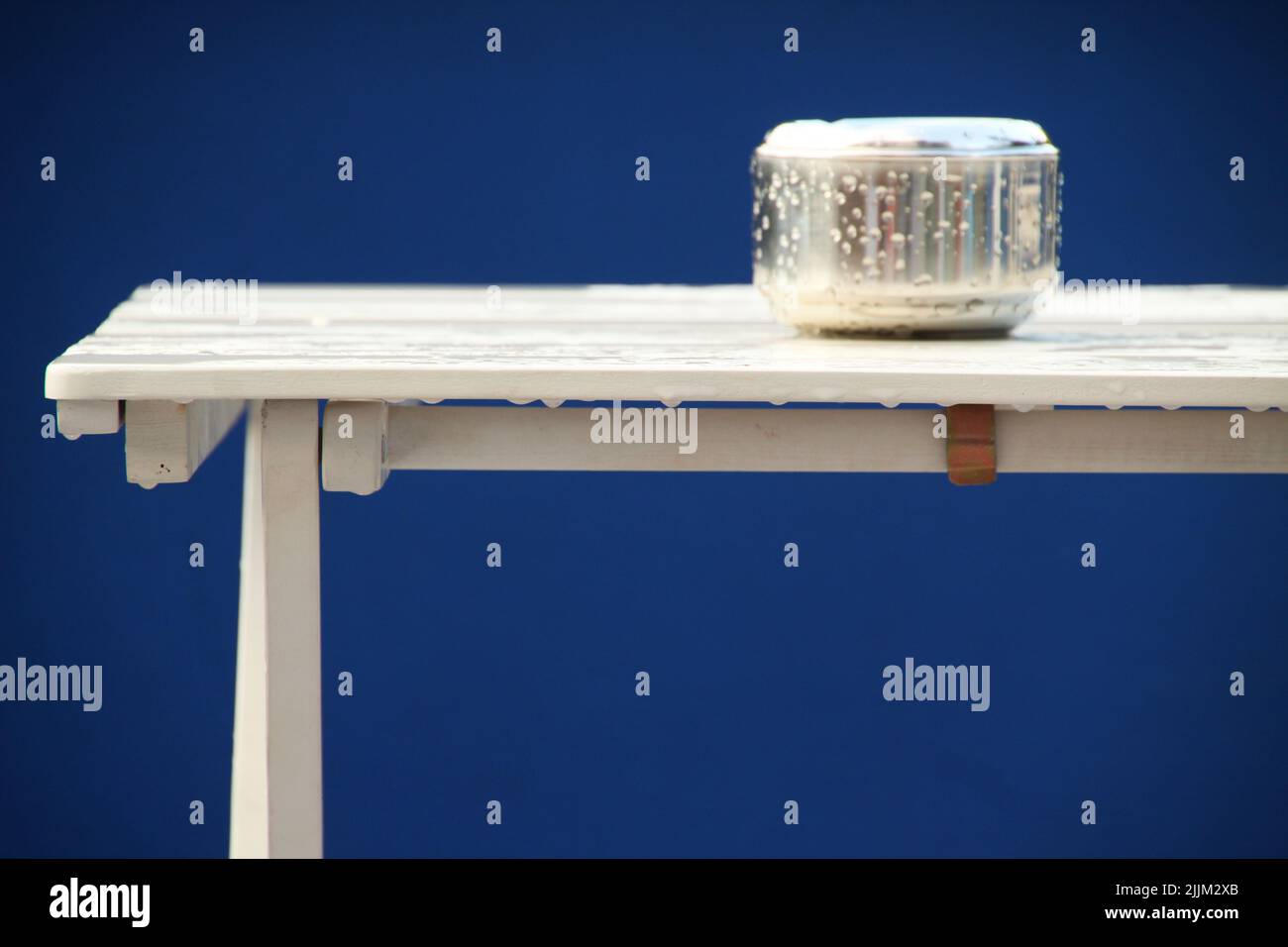 Ein nasser Aschenbecher auf einem nassen weißen Tisch vor blauem Hintergrund Stockfoto