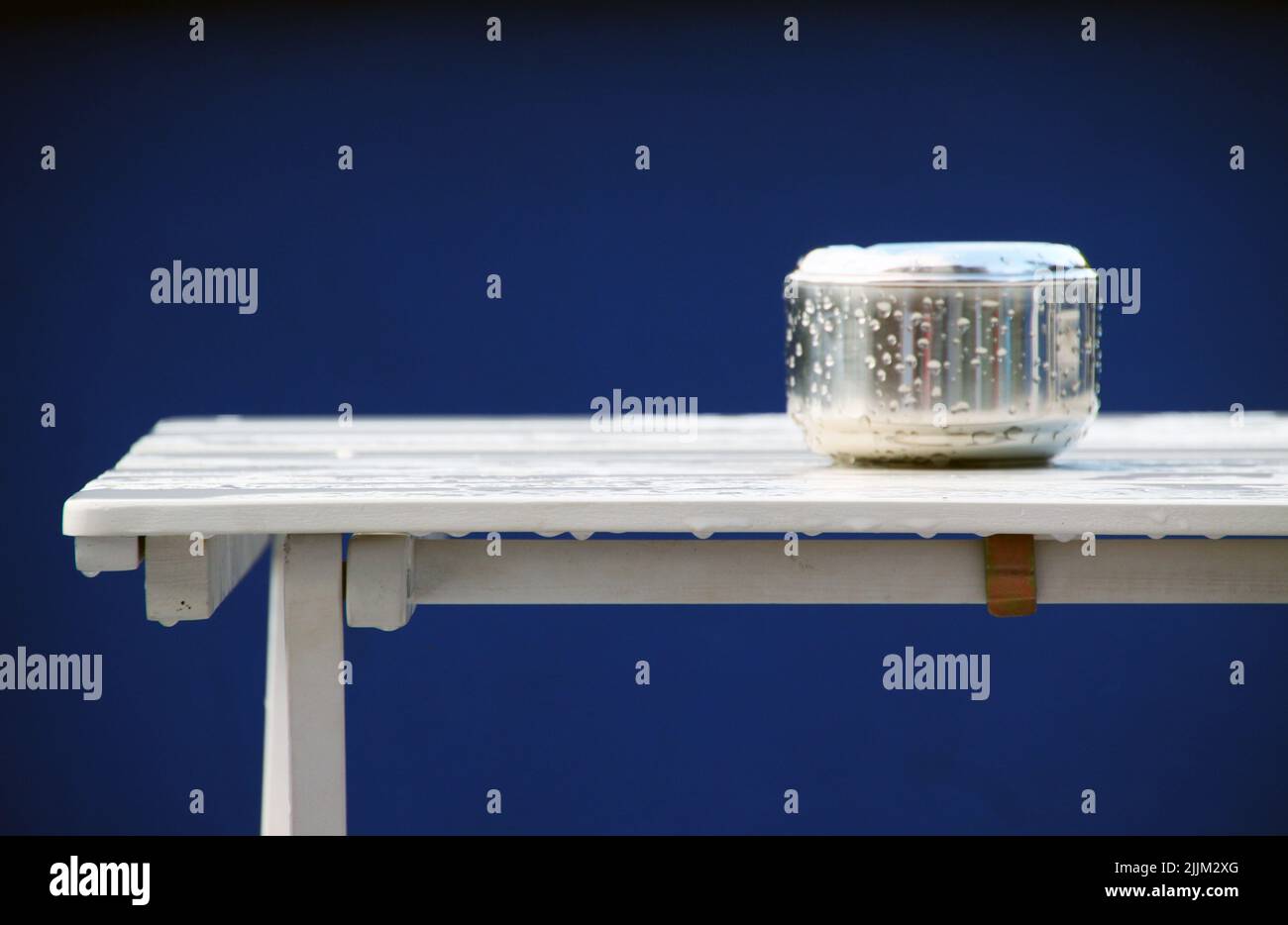 Ein nasser Aschenbecher auf einem nassen weißen Tisch vor blauem Hintergrund Stockfoto