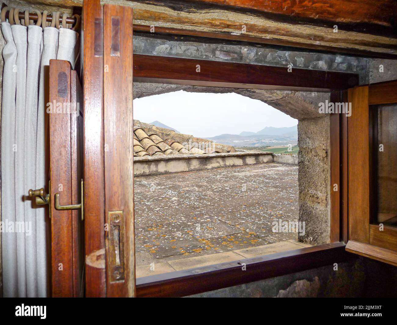 Ein Blick auf das Dach aus dem Fenster mit einem Holzrahmen eines alten Backsteinhauses in den Bergen Stockfoto