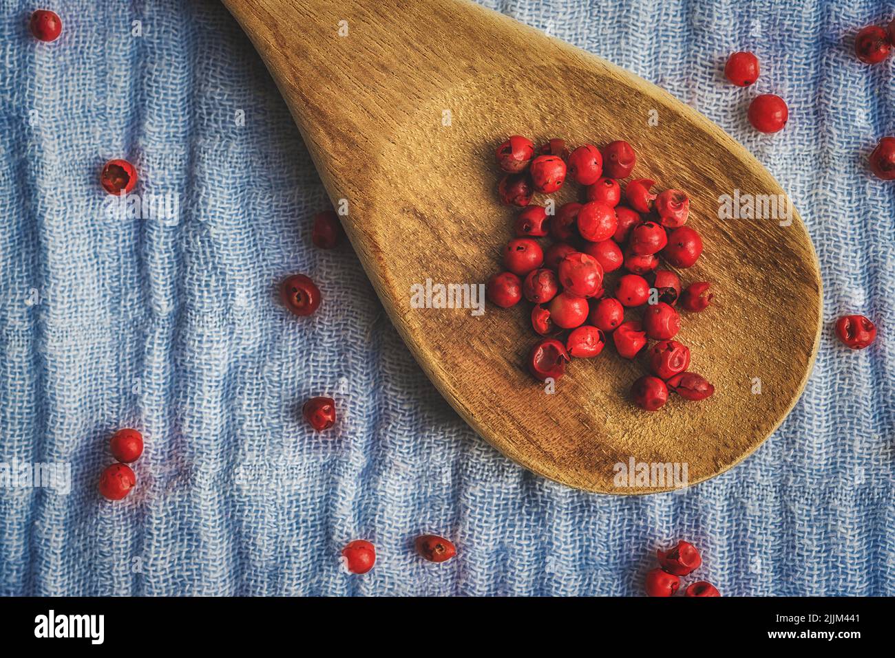 Draufsicht auf getrocknete rote Pfefferbällchen auf einem Holzlöffel und einer blauen Stoffoberfläche Stockfoto