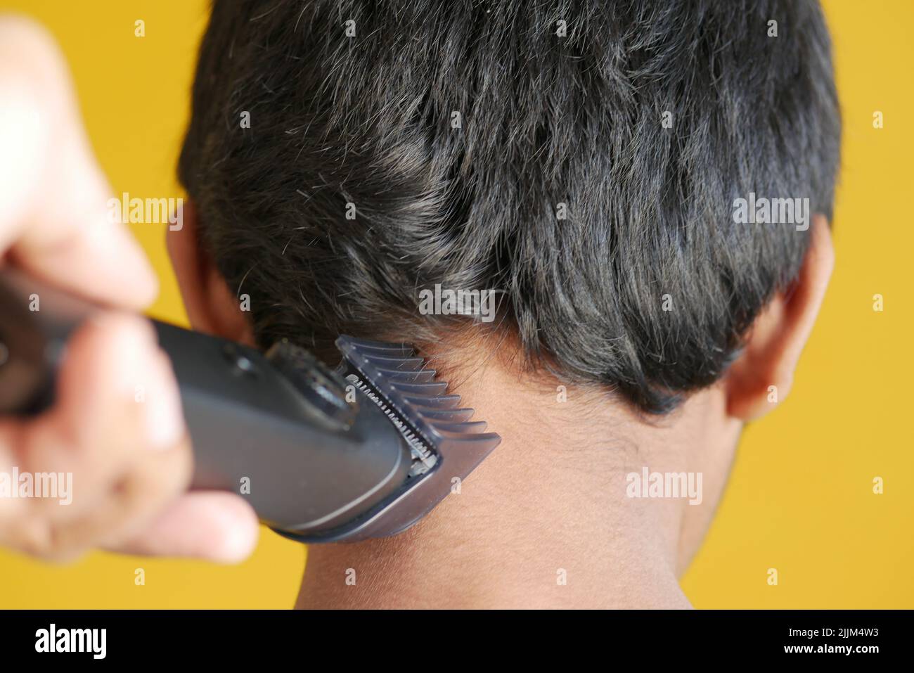 Schneiden Sie die Haare mit einem Haarschneider auf gelbem Hintergrund Stockfoto