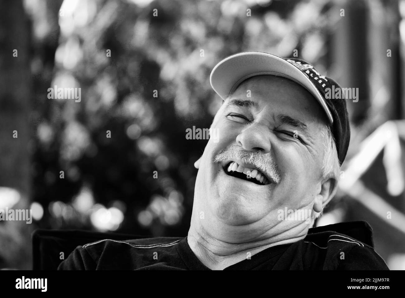 Eine Graustufen-Nahaufnahme eines lachenden Mannes mit Umhang. Stockfoto