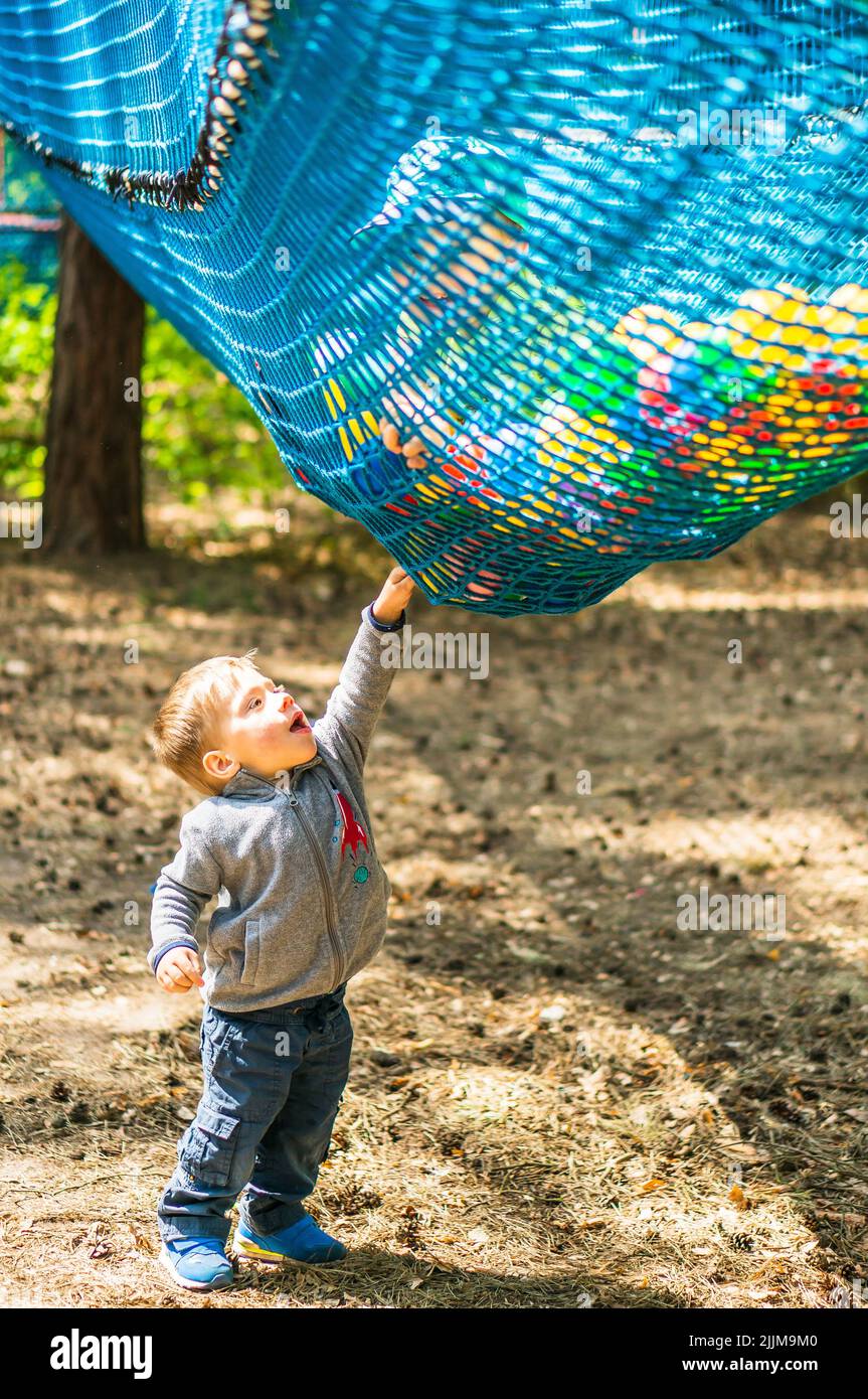 Eine vertikale Nahaufnahme eines kleinen Jungen, der ein Sicherheitsnetz mit Plastikkugeln einer Hindernisroute im Pyrland Park berührt. Stockfoto