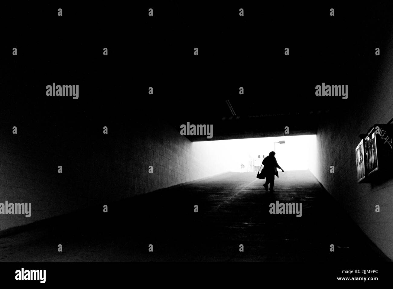 Eine Graustufenaufnahme einer Person, die in einem Tunnel mit einer Lichtquelle auf der anderen Seite läuft Stockfoto