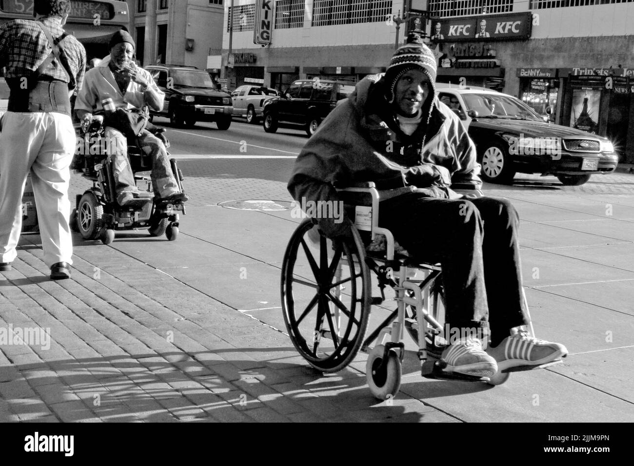 Ein Mann auf einem Rollstuhl, der in Graustufen durch die Straßen der Innenstadt von Los Angeles, Kalifornien, fährt Stockfoto