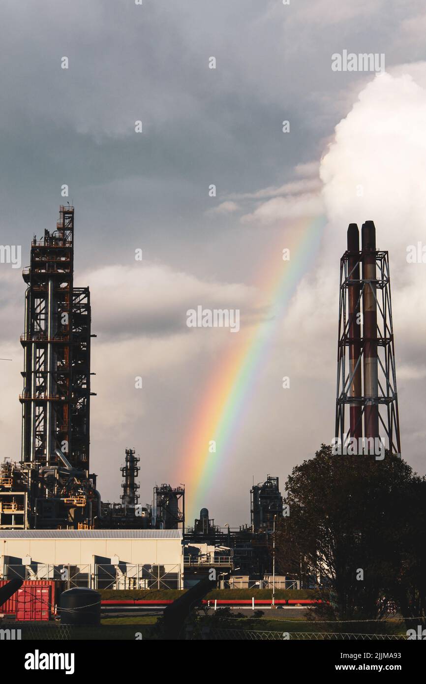 Eine vertikale Aufnahme eines Regenbogens über einem Industriegebiet mit Metalltürmen Stockfoto