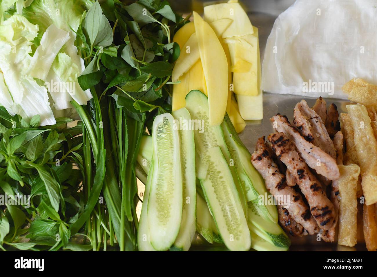 Frisches Gemüse mit in Scheiben geschnittenen unreifen Mango und gebratenem Fleisch auf dem Tisch, bereit zum Kochen von Frühlingsrollen Stockfoto