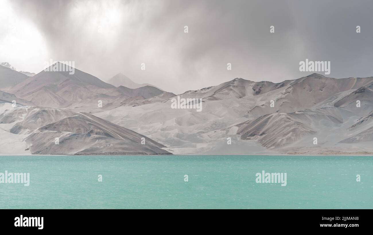 Ein See mit klarem Wasser, umgeben von salzigen Hügeln unter einem wolkigen Himmel Stockfoto