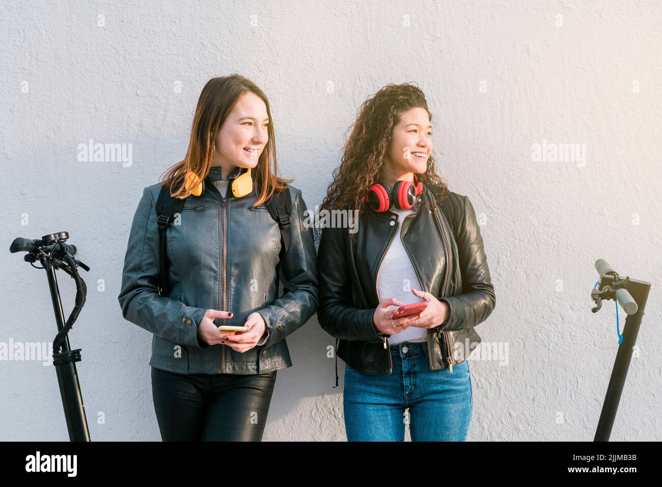Zwei multiethnische Freundinnen auf Elektrorollern mit Smartphone im Freien Stockfoto