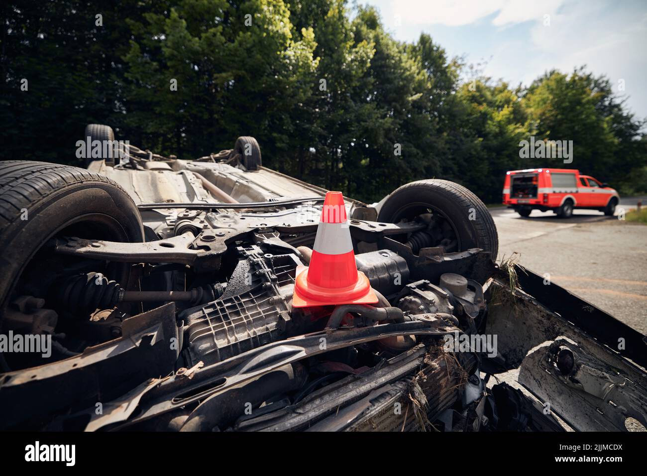 Beschädigtes Fahrzeug auf dem Dach nach einem Unfall mit einem Feuerwehrfahrzeug. Selektiver Fokus auf den Verkehrskegel. Stockfoto
