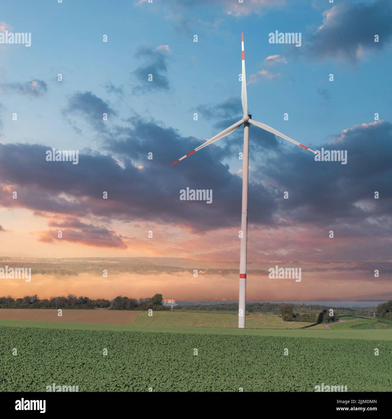 Eine malerische Aussicht auf eine Windmühle in einem offenen grünen Feld bei einem schönen bewölkten Sonnenuntergang Stockfoto