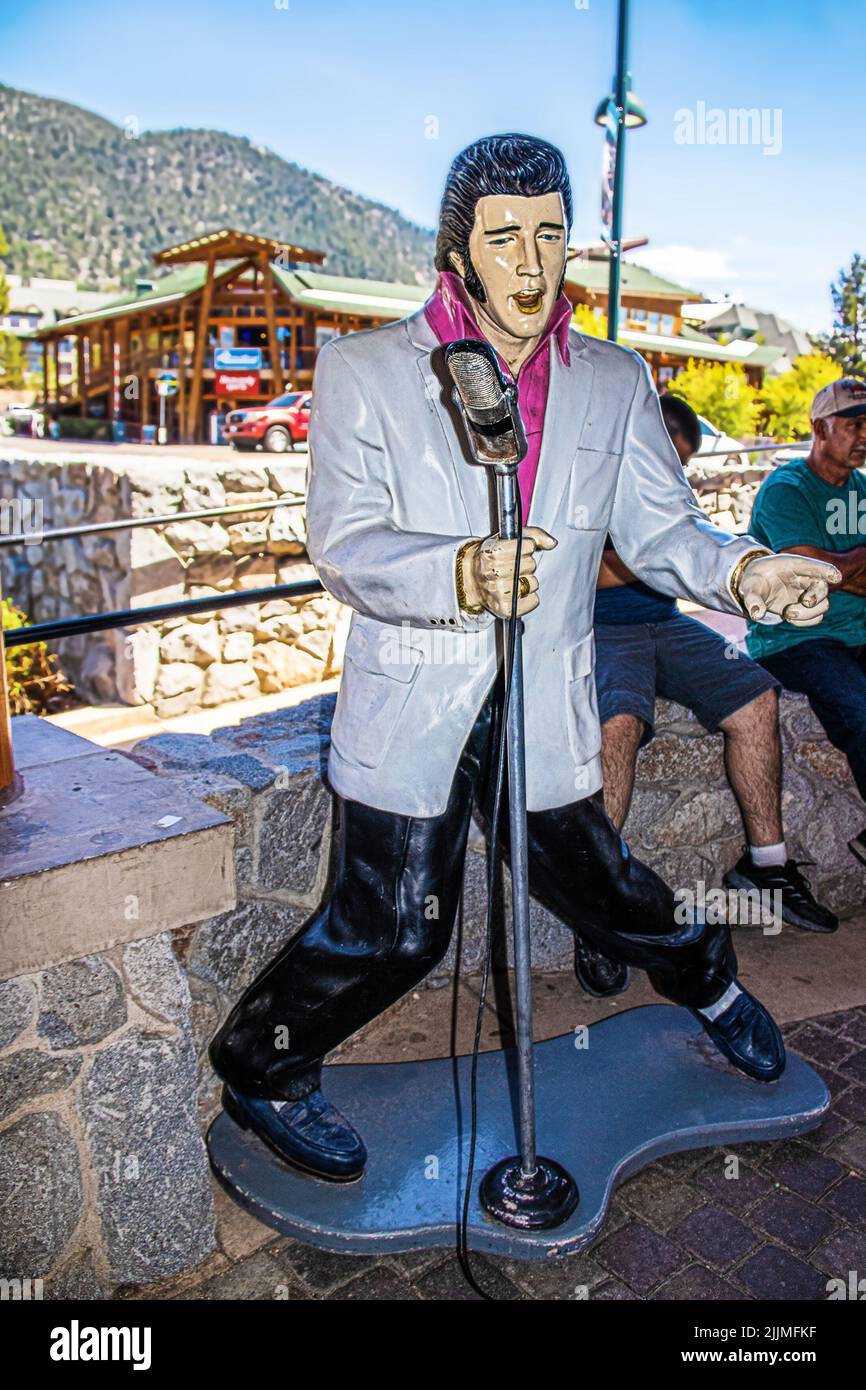 2021-06-01 South Tahoe USA - Statue von Elvis, der mit Mikrofon und blauen Wildlederschuhen auf der Seitenwand in South Tahoe singt, mit Touristen, die auf einer Felswand sitzen Stockfoto