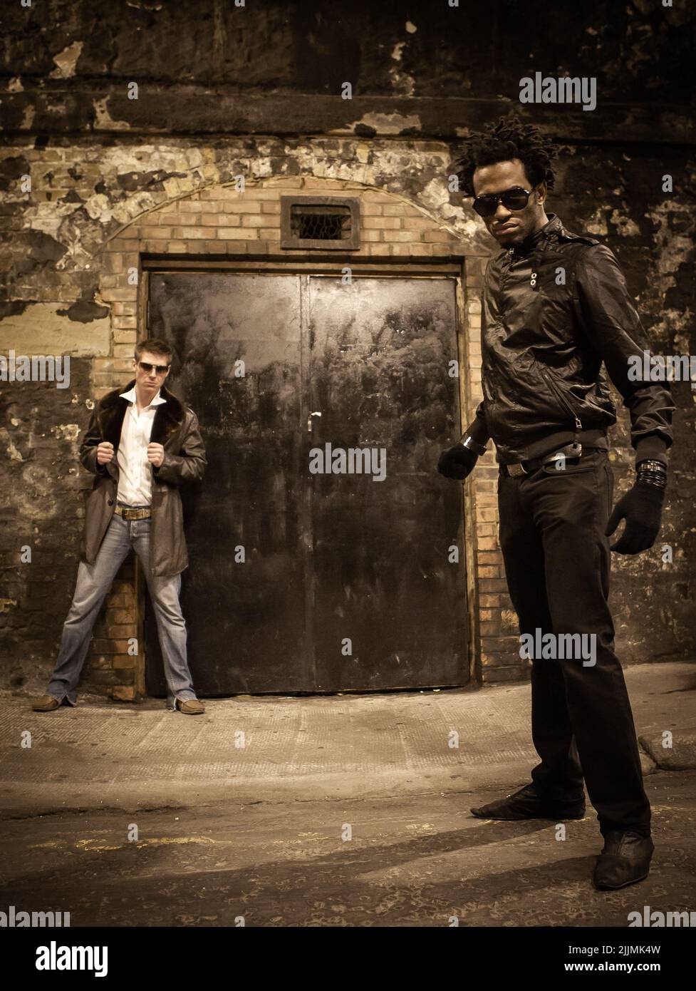 Türsicherheit. Ein Paar Sicherheitskräfte im Nachtclub, die an einem anonymen Eingang in einer städtischen Umgebung Wache halten. Aus einer Serie mit den gleichen Modellen. Stockfoto