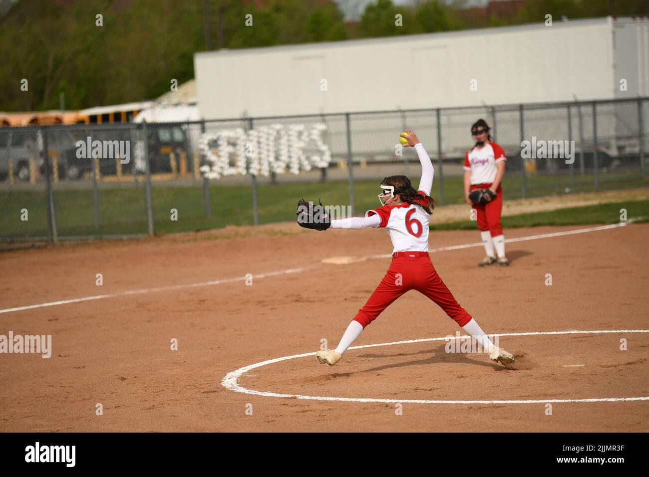 Ein Mädchen in einer rot-weißen Uniform, das den Ball während des Softball-Spiels fängt Stockfoto