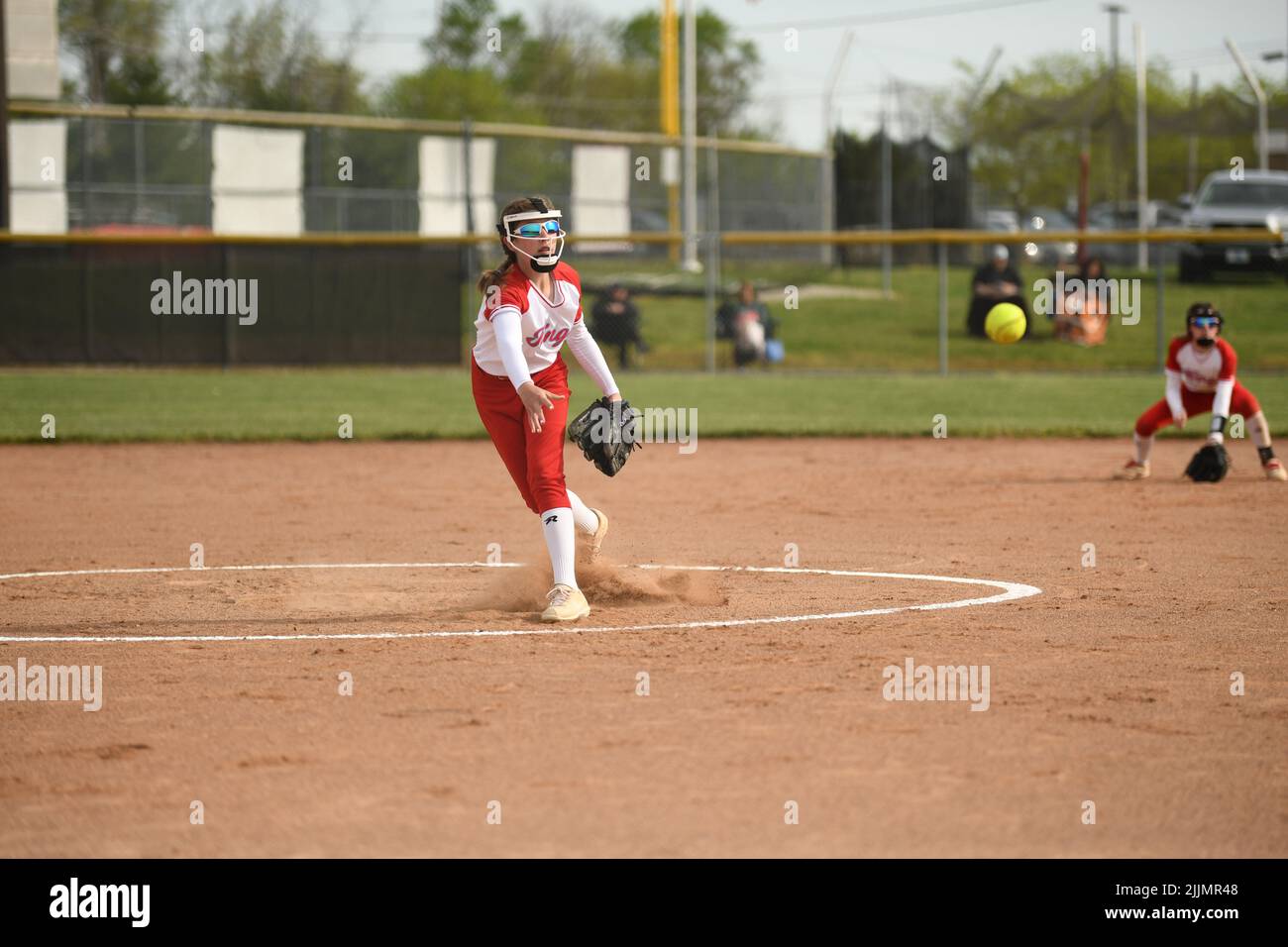 Ein Mädchen in einer rot-weißen Uniform, das den Ball während des Softball-Spiels fängt Stockfoto