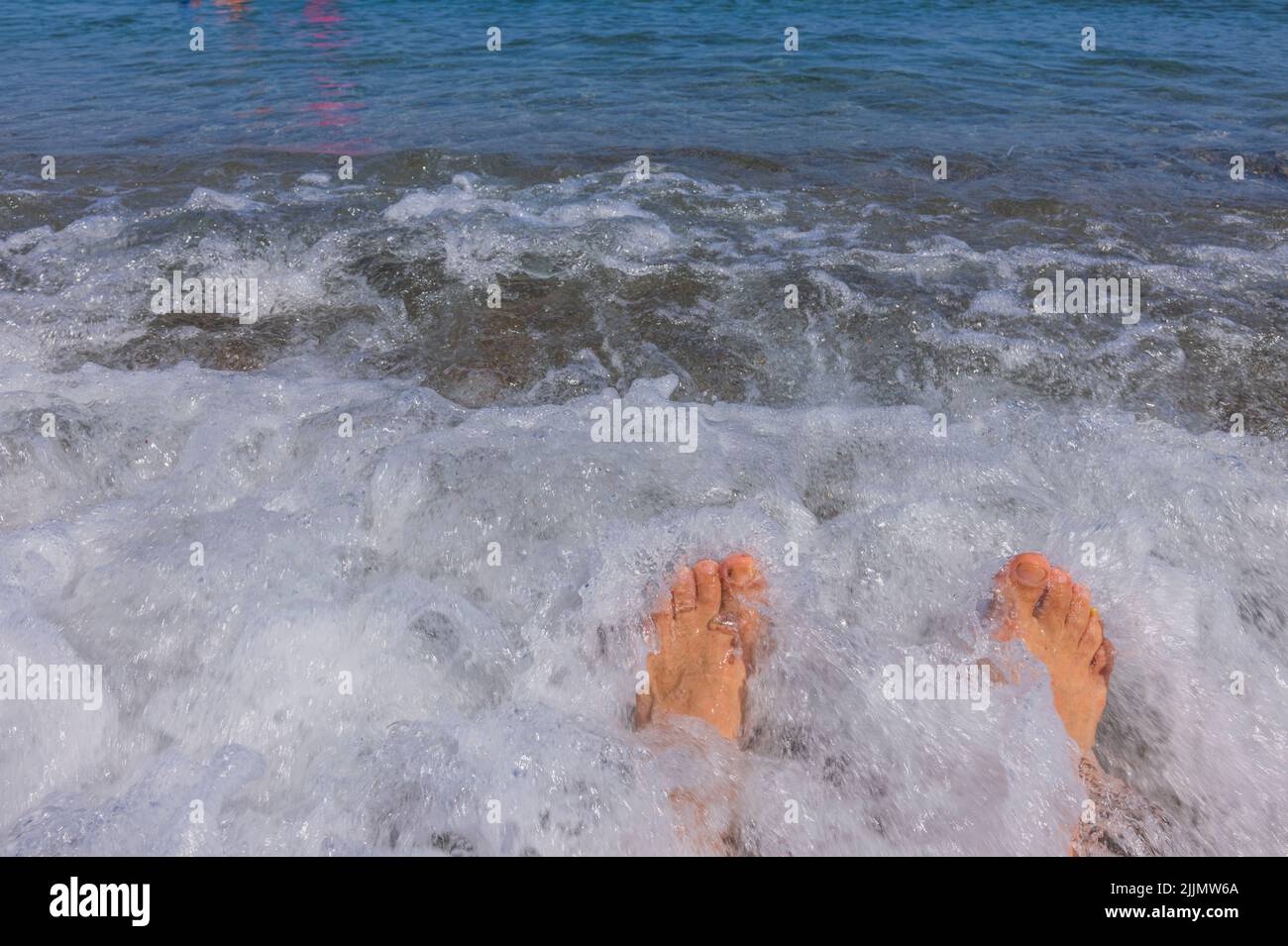 Schöne Ansicht der männlichen Beine an der Küste während der rollenden Welle. Konzept für Sommerferien. Stockfoto