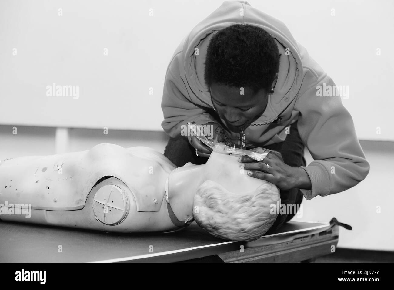 Eine Graustufenaufnahme einer Person, die eine erste-Hilfe-CPR-Schulung mit einem Plastikdummy durchführt Stockfoto