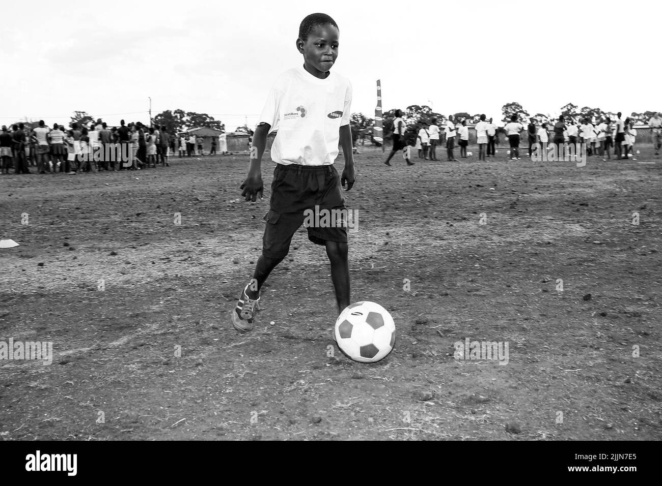 Eine Graustufe eines afrikanischen Kindes, das auf dem Schulhof in Johannesburg, Südafrika, Fußballaktivitäten unternimmt Stockfoto