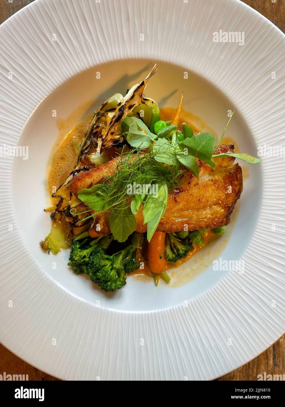 Blick von oben auf gebratenen Fisch mit Brokkoli, Karotten, Kohl, Erbsensprossen und Buttersauce Stockfoto