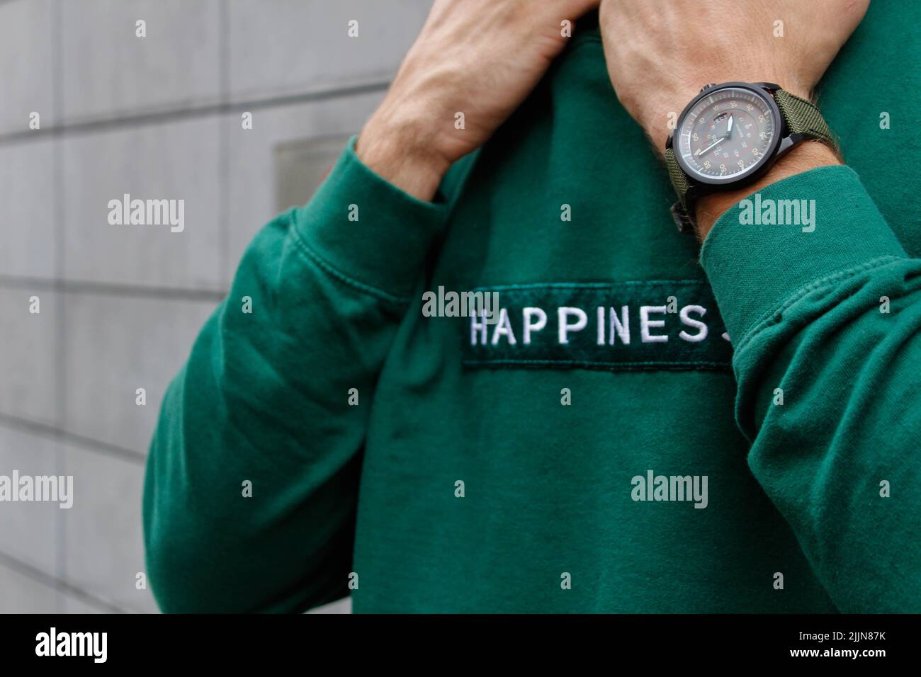 Eine Nahaufnahme eines Mannes mit einer Uhr in einem grünen Happiness Hoodie Stockfoto