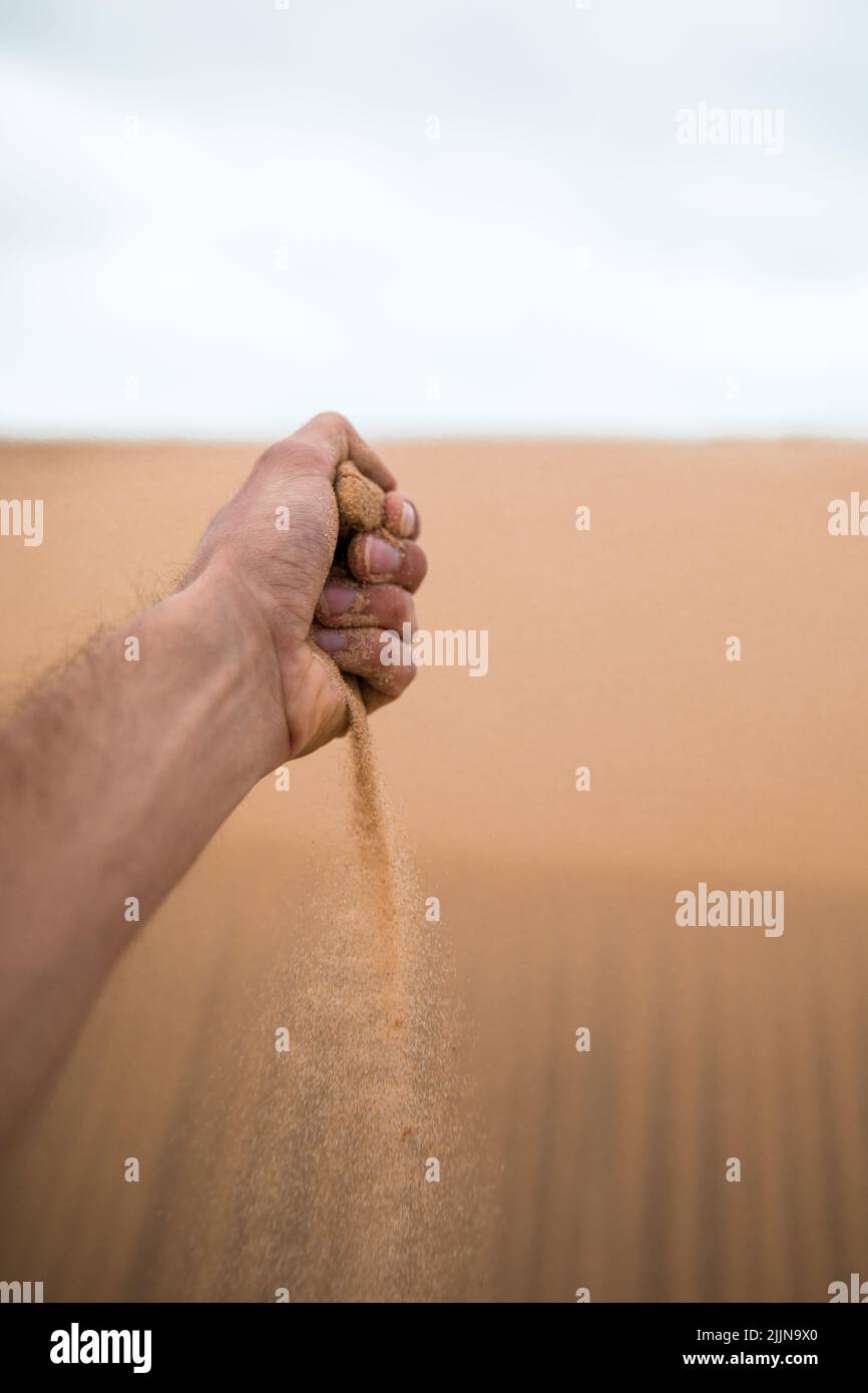 Eine Nahaufnahme einer Hand, die goldenen Sand umklammert, der in Bordeaux, Frankreich, durchfällt Stockfoto