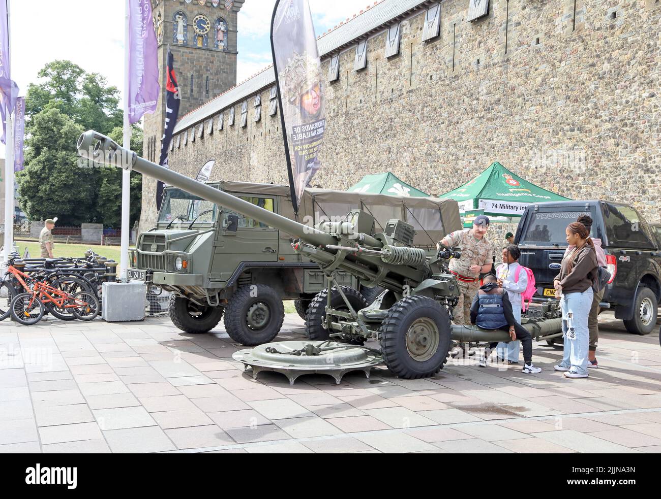Soldat, der der ethnischen Familiengruppe eine große Waffe/Kanone zeigt. Rekrutierungsstände der Streitkräfte, Central Cardiff, Juli 2022. Sommer. Stockfoto