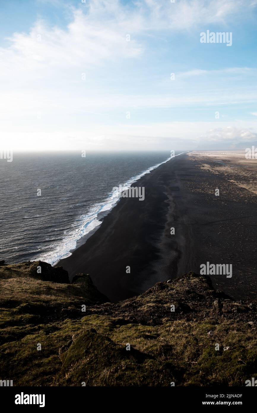 Eine malerische Aussicht auf den Kirkjufjara-Strand gegen den blau bewölkten Himmel in hellem Sonnenlicht in Südisland Stockfoto