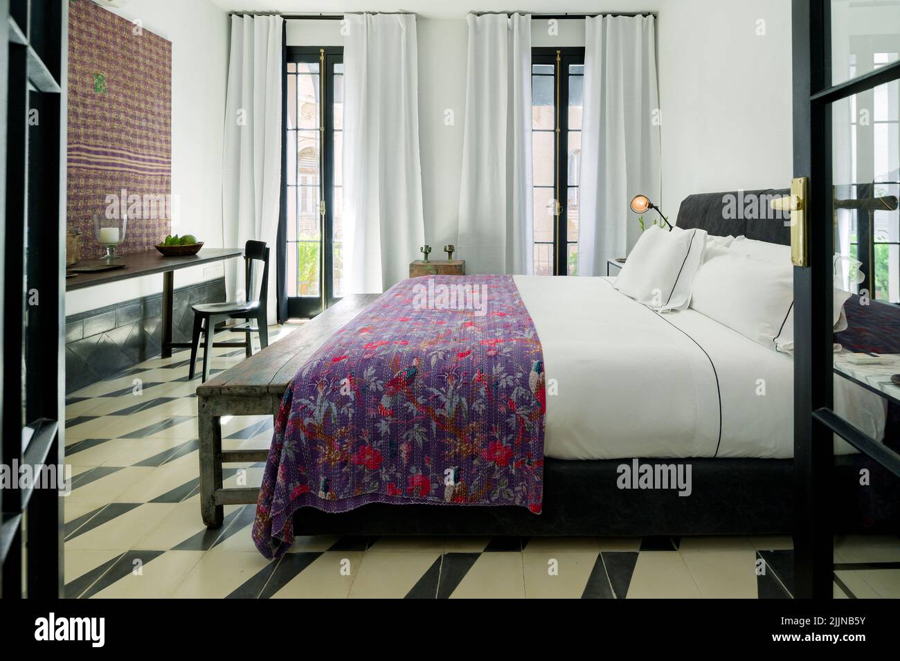 Ein Schlafzimmer mit einem eklektischen Design mit einem bequemen Bett und Zugang zum Balkon. Stockfoto