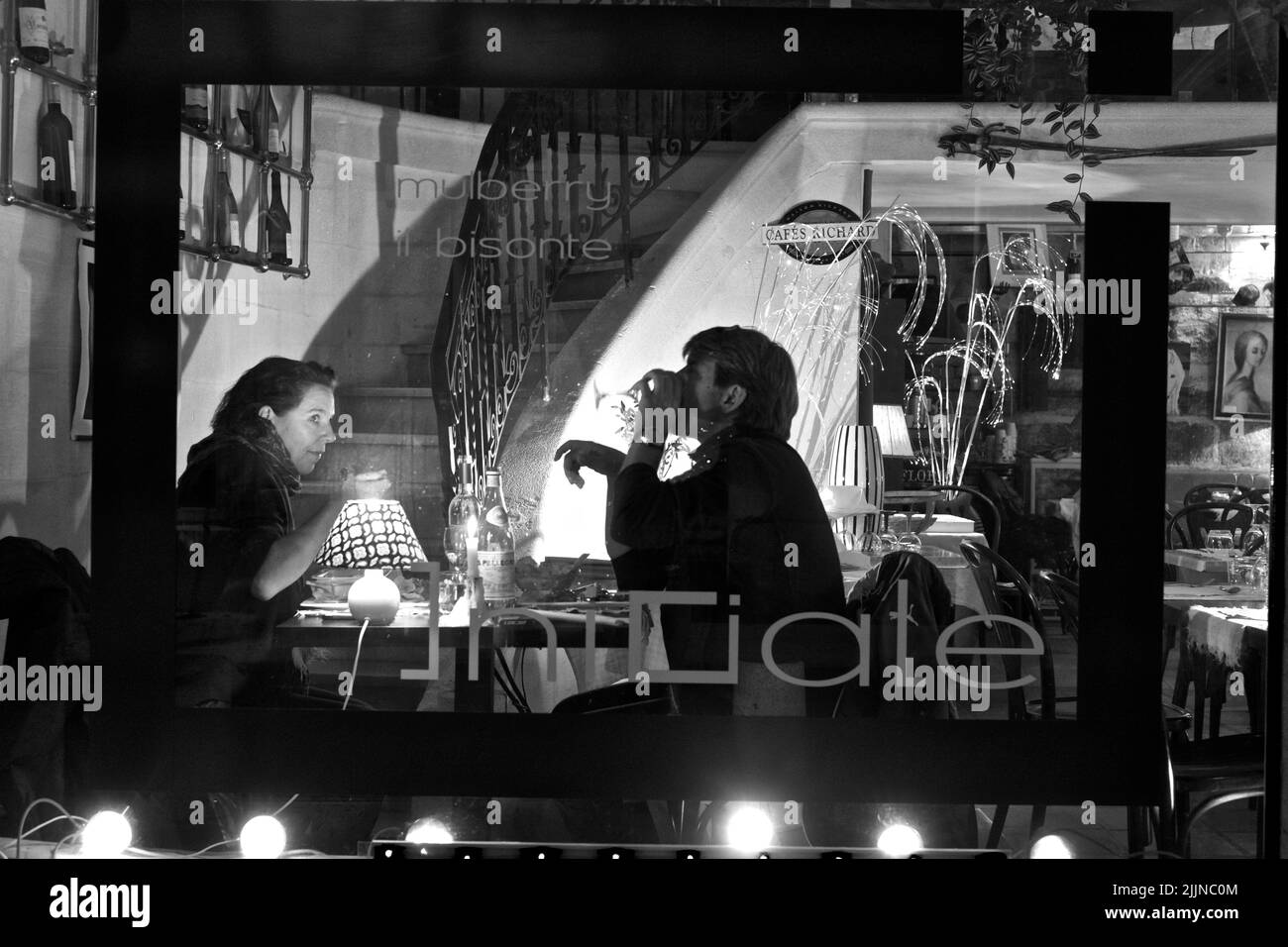 Eine Graustufe eines romantischen Paares, das in einem Café in Frankreich einen Drink zu sich nehmen kann Stockfoto
