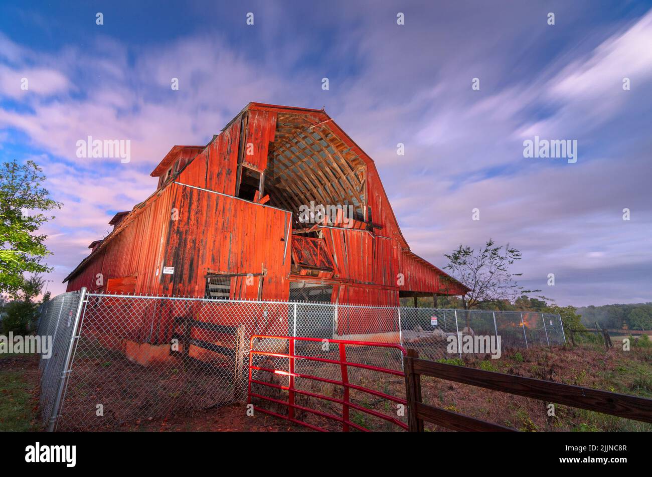 Eine alte rote Scheune in Ruinen in einer ländlichen Umgebung in der Dämmerung. Stockfoto
