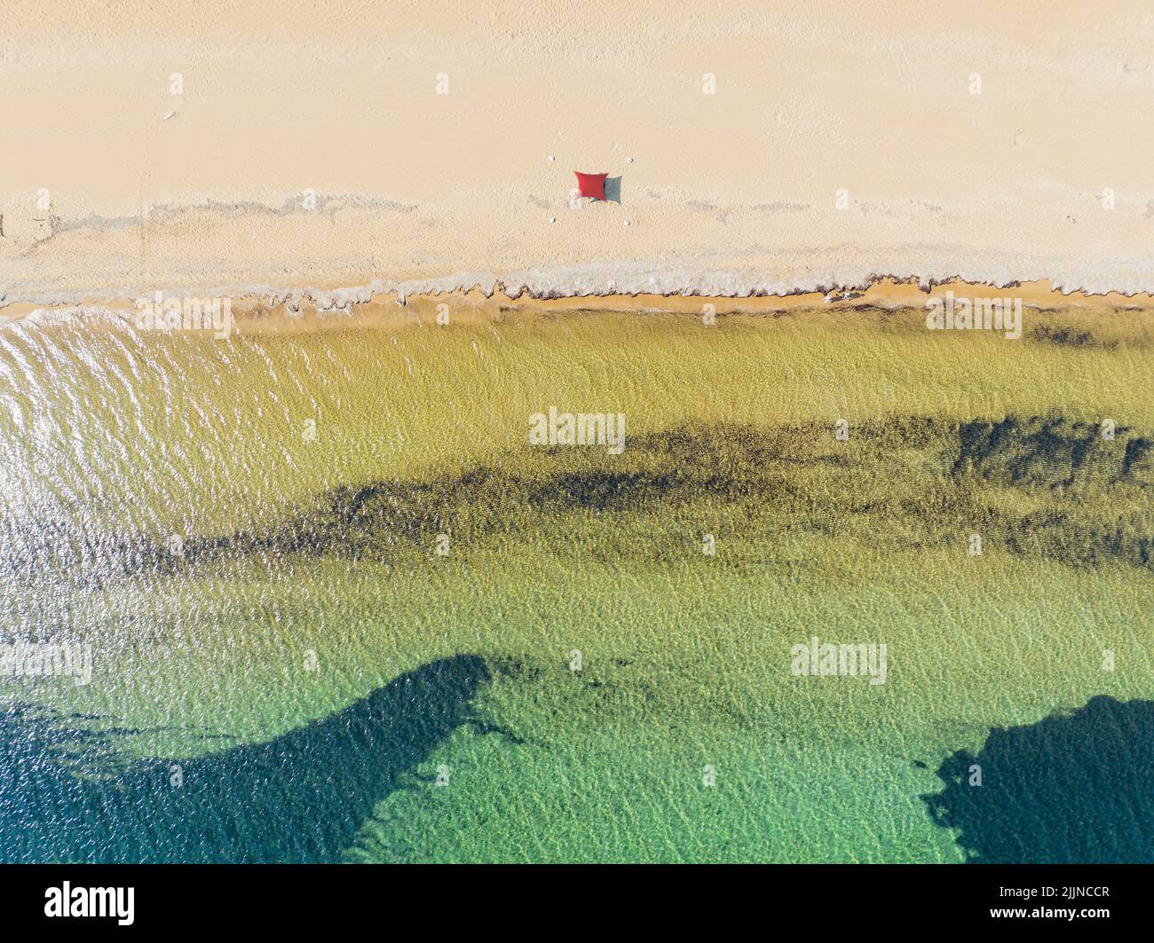 Luftaufnahme des Strandes von Paralia Issos in Korfu, Griechenland. Markise. Rotes Strandzelt. Badegäste, die am Ufer spazieren Stockfoto