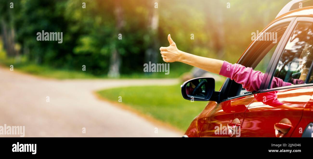 woman inside car on the road trip with thumb up gesture out of the window. banner with copy space Stockfoto