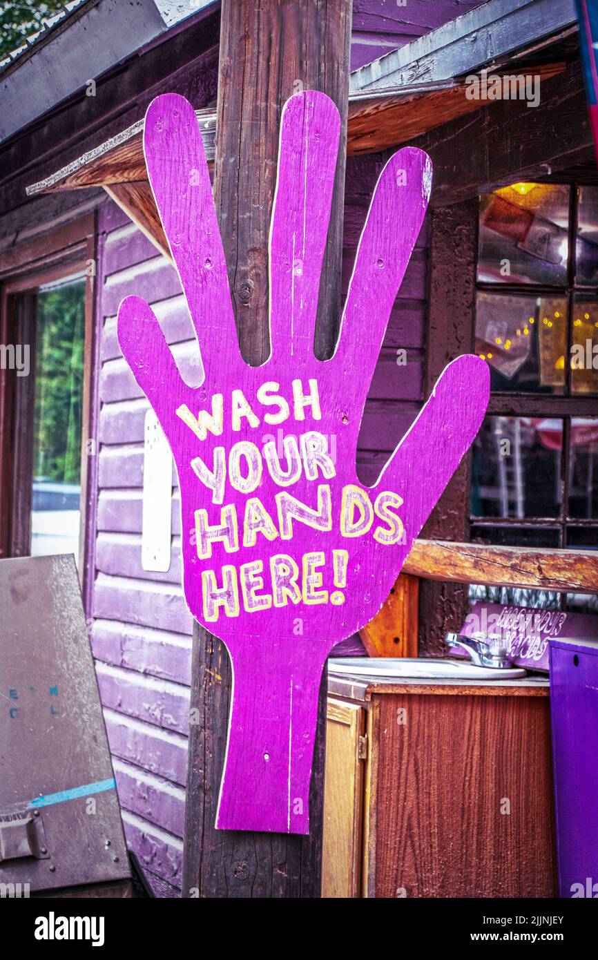 Riesiges Holz-Fushia-Ausschnitt-Handschild liest Wash your Hands here by small sink outside purple sided Cabin Business in Talkeetna Alaska Stockfoto